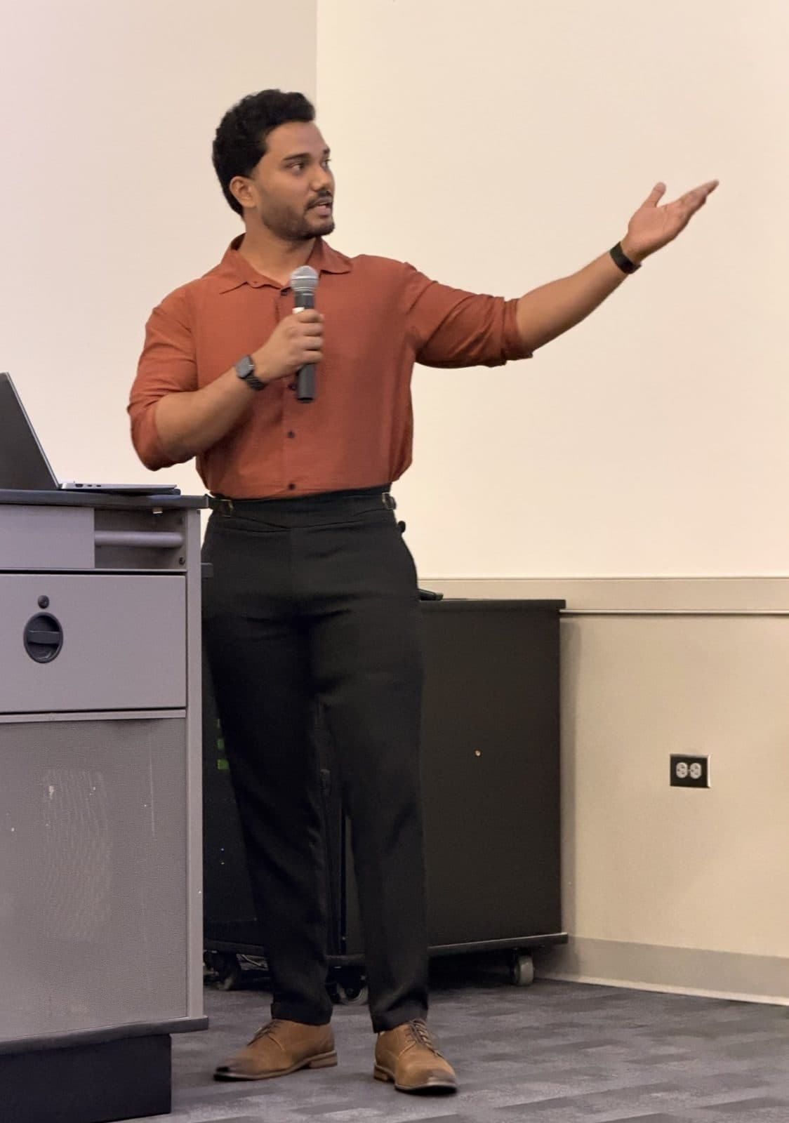 Manikanta gesturing toward the audience while presenting